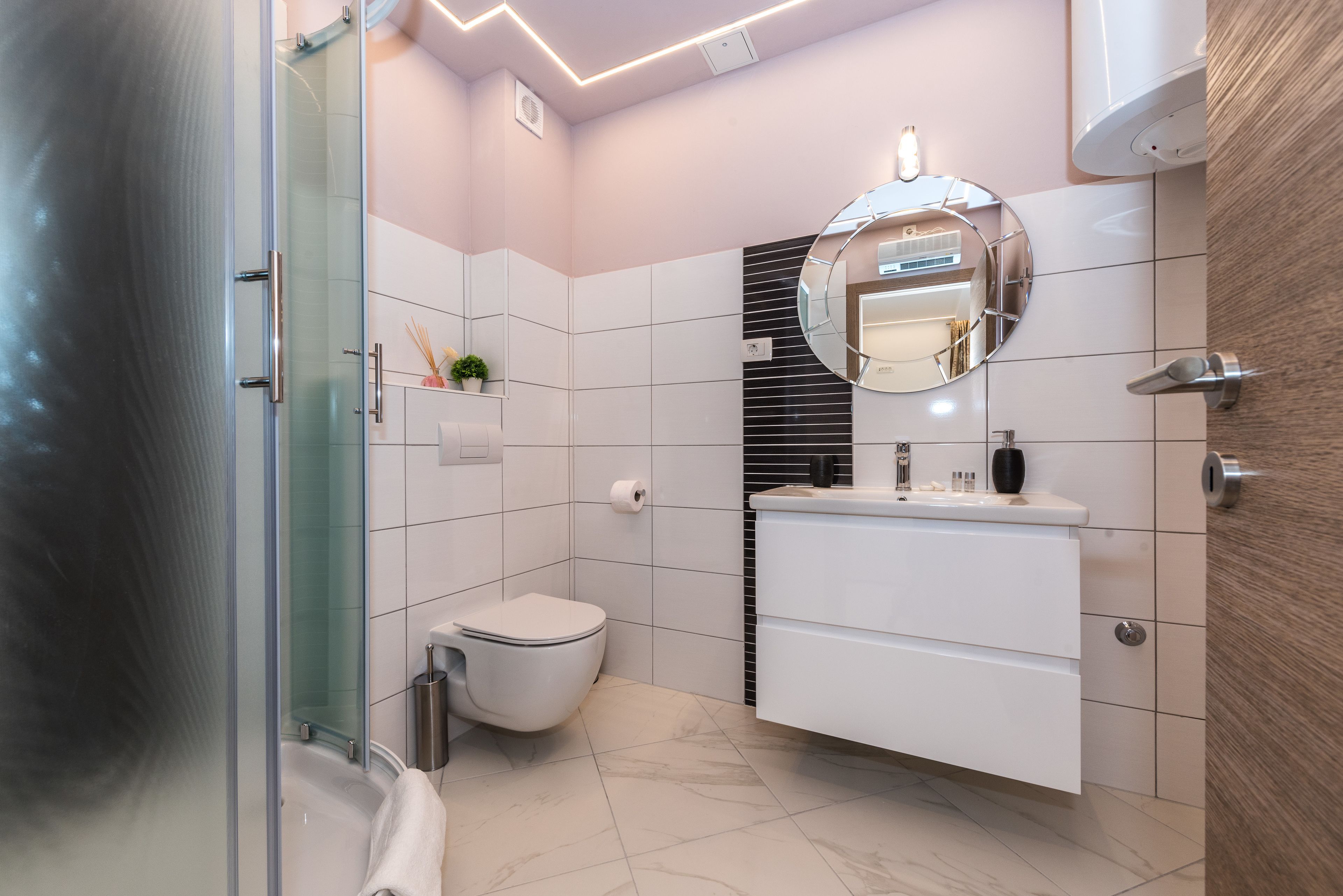 A modern bathroom with a glass shower enclosure, a white toilet, a vanity with a mirror, and a towel rack.