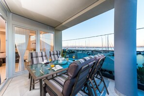 A balcony with a glass table and chairs, a view of the marina, and a glass door leading to an indoor area.