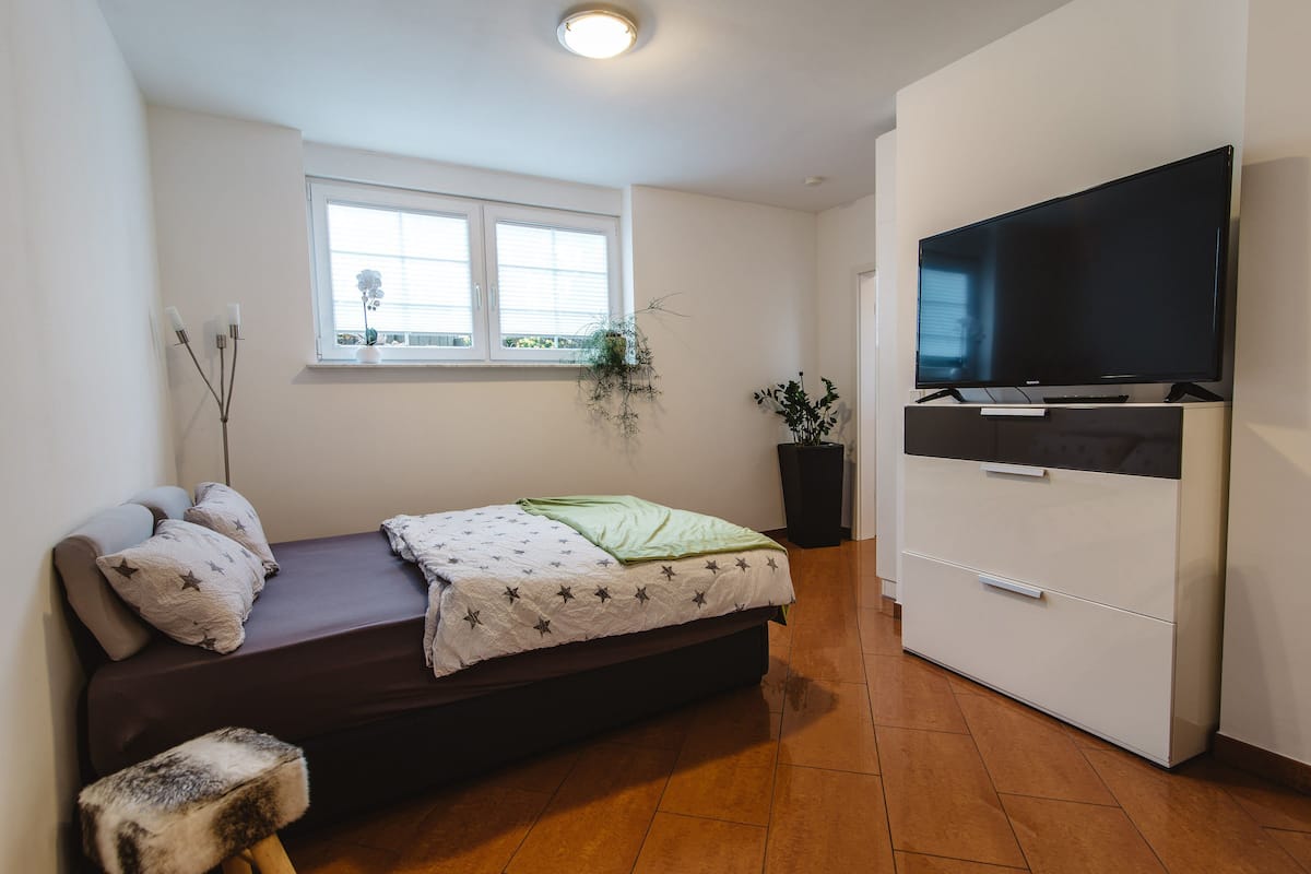Een compacte, moderne slaapkamer met een bed, een televisie en een raam.