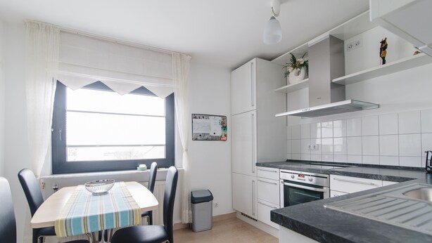 Une cuisine moderne avec des meubles blancs, un plan de travail noir et un coin repas comprenant une table et des chaises.