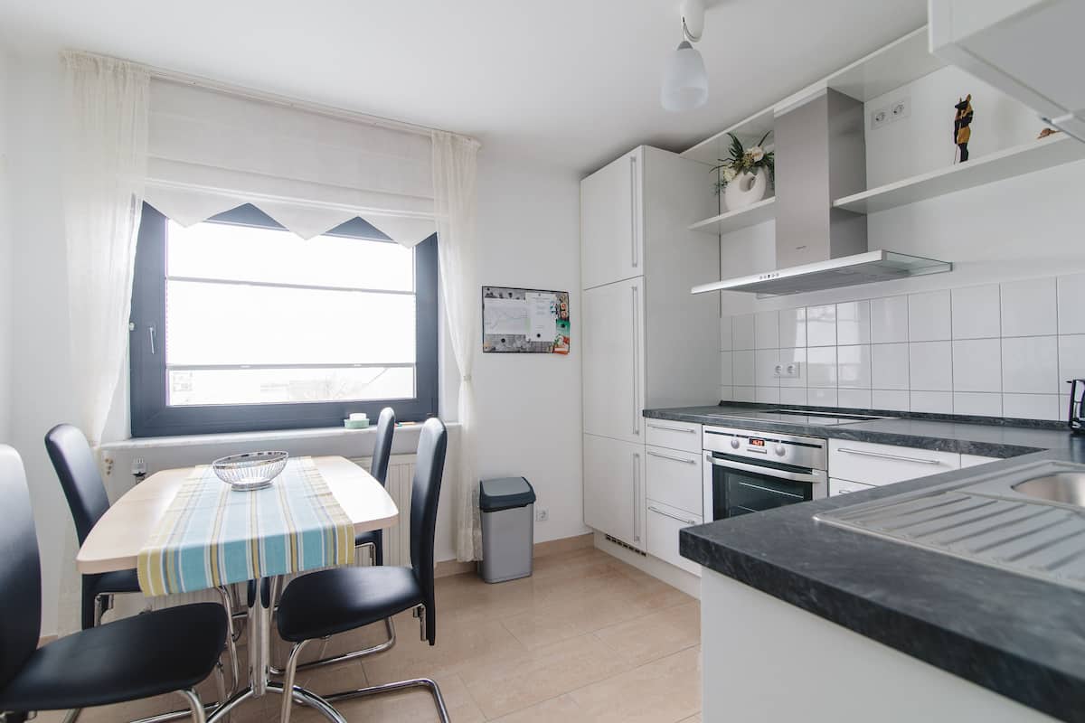 Een moderne keuken met witte kastjes, een zwart aanrecht en een eethoek met een tafel en stoelen.
