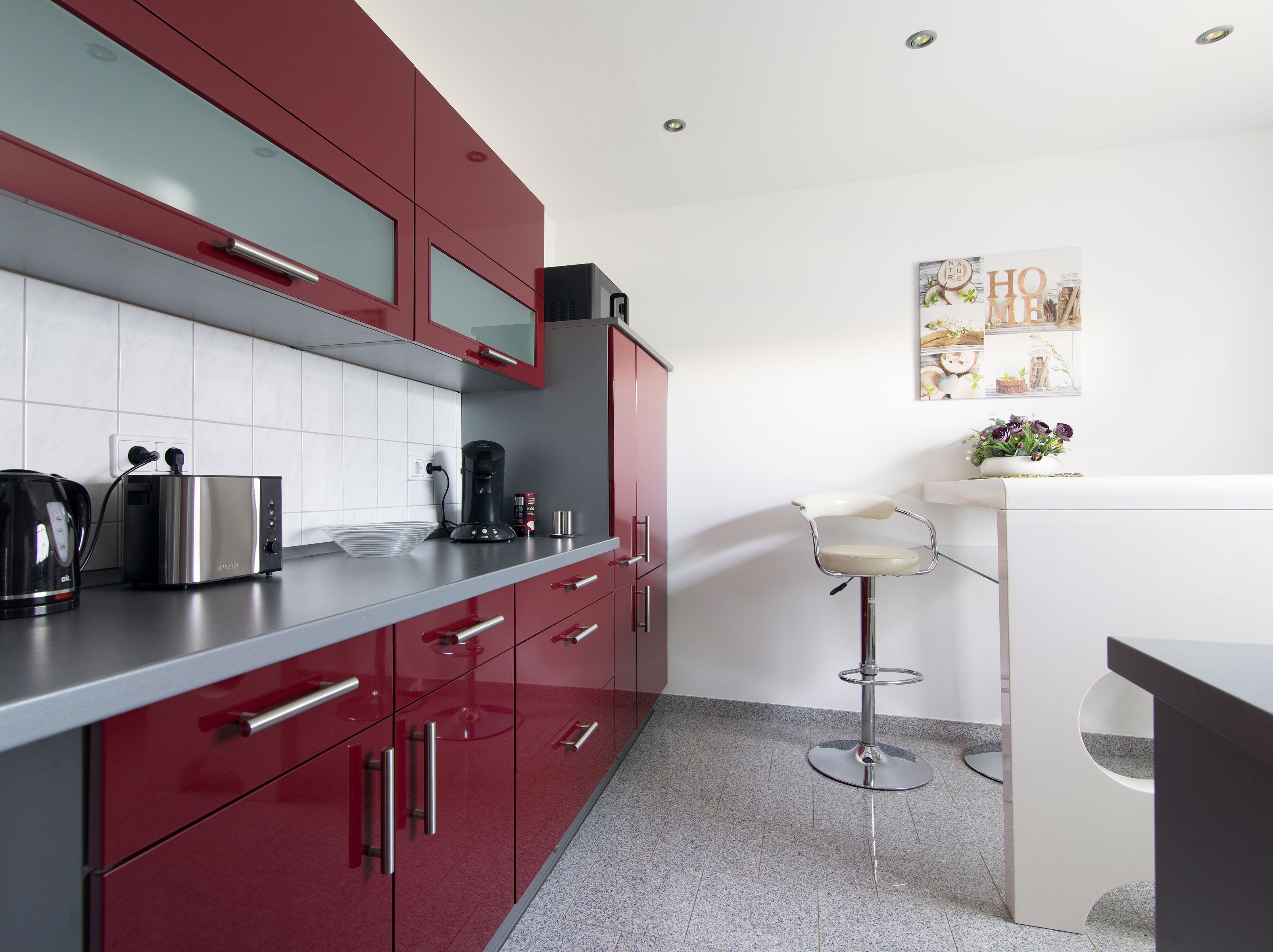 A modern kitchen with red cabinets, stainless steel appliances, and a bar stool.