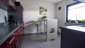 Une cuisine moderne avec des meubles de rangement rouges, un réfrigérateur blanc, une machine à café et un tabouret de bar.
