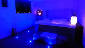 A room with a hot tub, a small table, and a bench. - La Douce Escapade (Sizun)