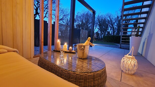 A cozy outdoor seating area with a wicker table, candles, and a champagne bottle. - La Douce Escapade (Sizun)