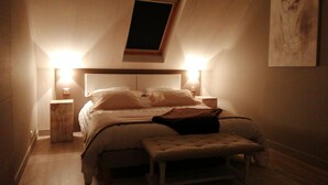 A bedroom with a sloped ceiling, a bed with pillows, a bedside table, a nightstand, and a painting on the wall. - La Douce Escapade (Sizun)