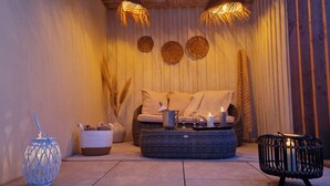 A cozy seating area with a wicker sofa, candles, and a basket of slippers. - La Douce Escapade (Sizun)