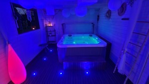 A small, dimly lit room with a hot tub, a small table, and a shelf with items. - La Douce Escapade (Sizun)