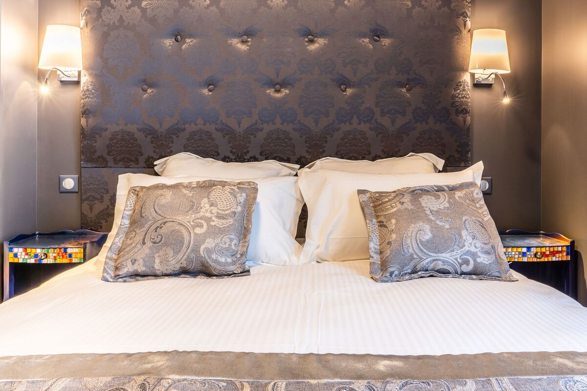 Een bed met een gestoffeerd hoofdeinde, twee bedlampen en gestreepte kussens.