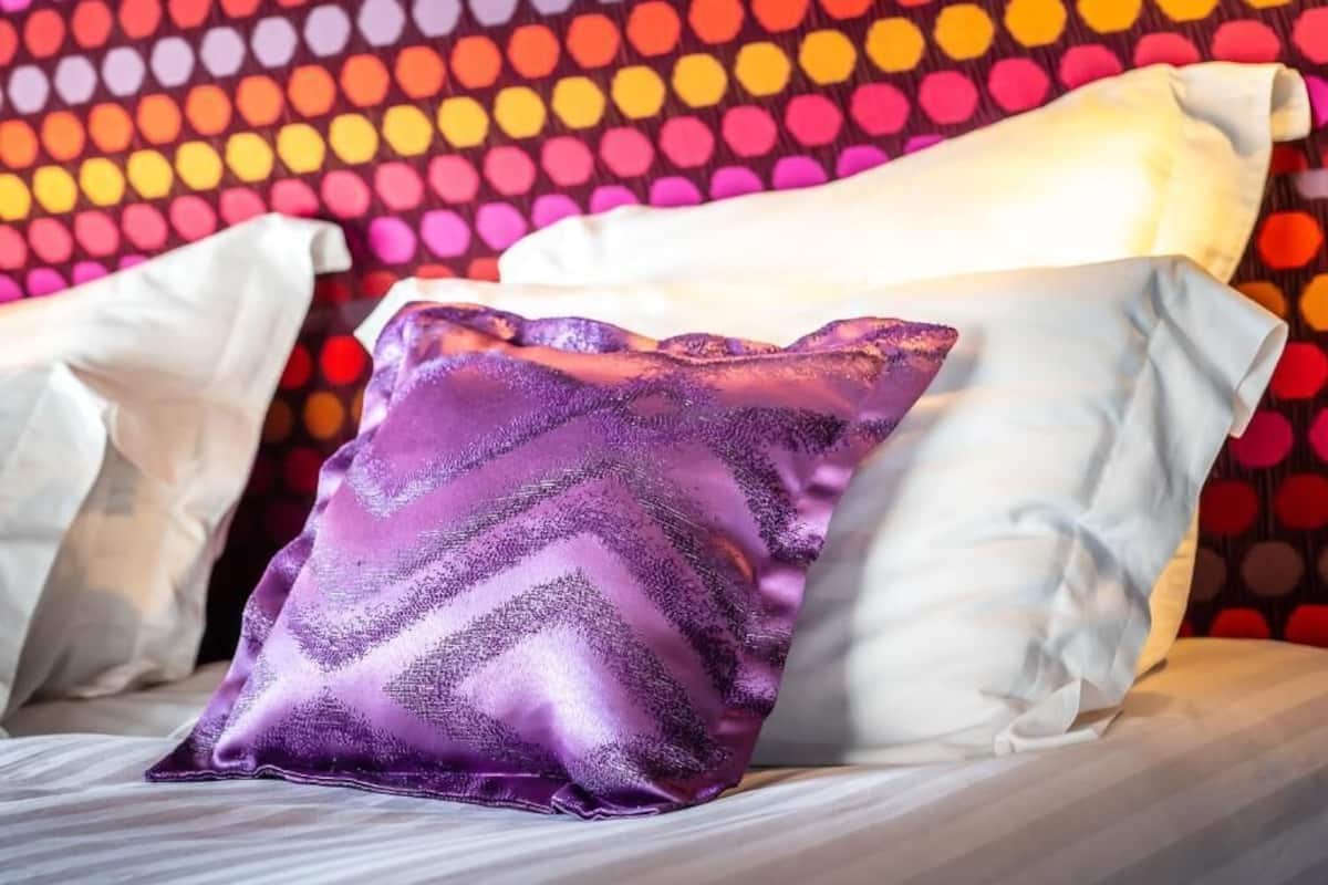 A bed with white pillows and a single purple pillow with a chevron pattern.