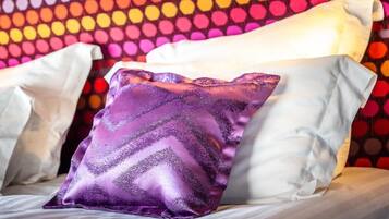 A bed with white pillows and a single purple pillow with a chevron pattern.