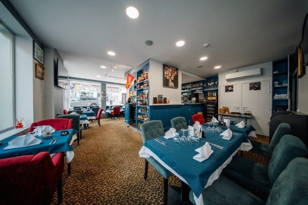 En restaurant med borde dækket til spisning, et barområde og hylder fyldt med flasker.