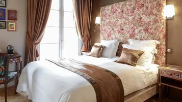 Una cama bien hecha con un cabecero floral, una mesita de noche con una lámpara y una silla con un cojín colorido.