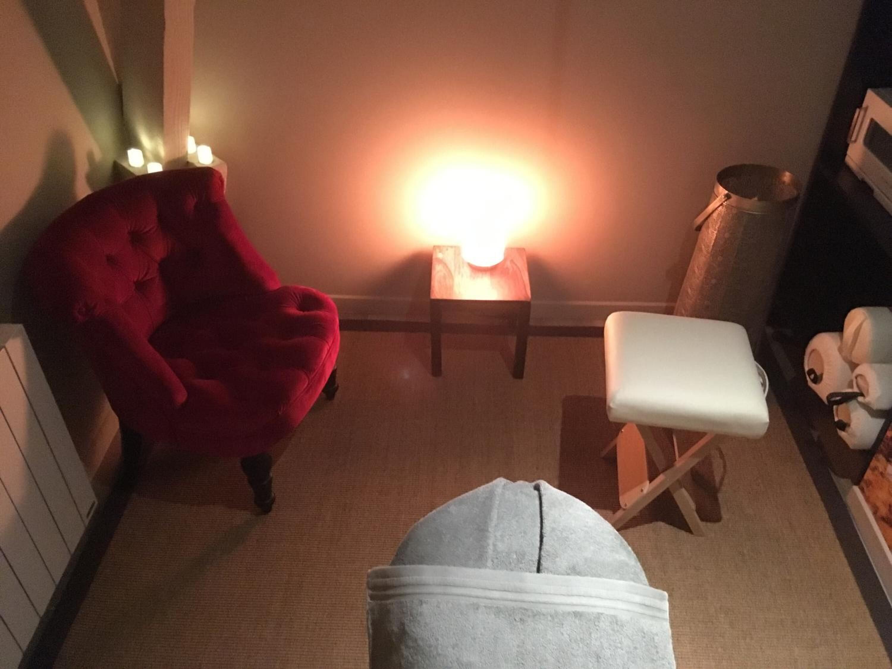 A cozy room with a red armchair, a small table with a lamp, a white bench, and a white bathtub.