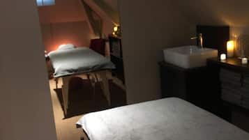 Una camera da letto con un letto, un comodino, una piccola finestra e un bagno con un lavandino e uno specchio.