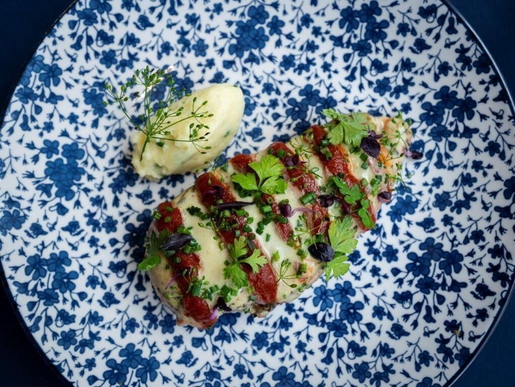 A plate with a fish fillet topped with herbs and sauce, and a side of mashed potatoes.