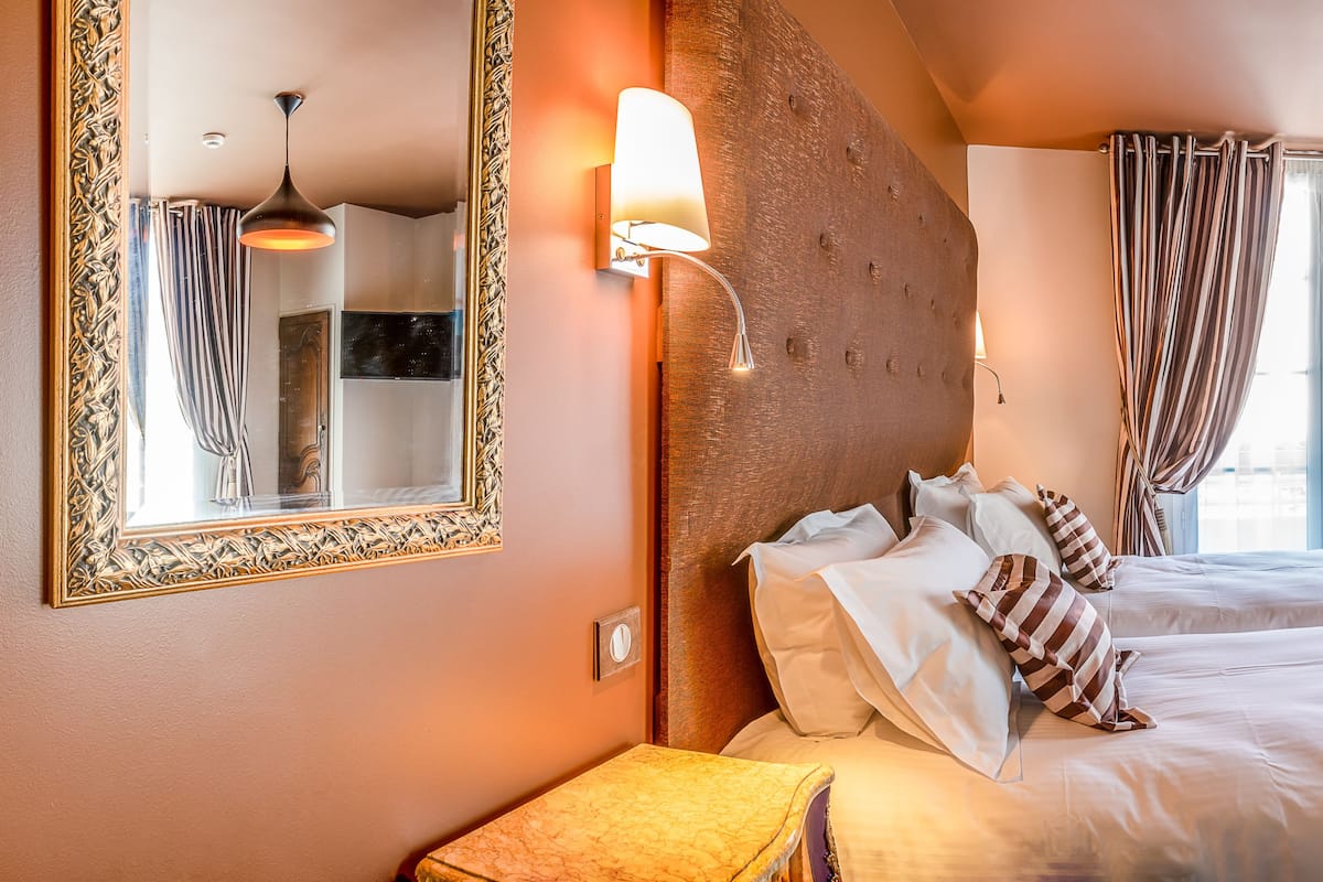 A hotel room with two beds, a large mirror, a wooden headboard, and a view of the city through the windows.