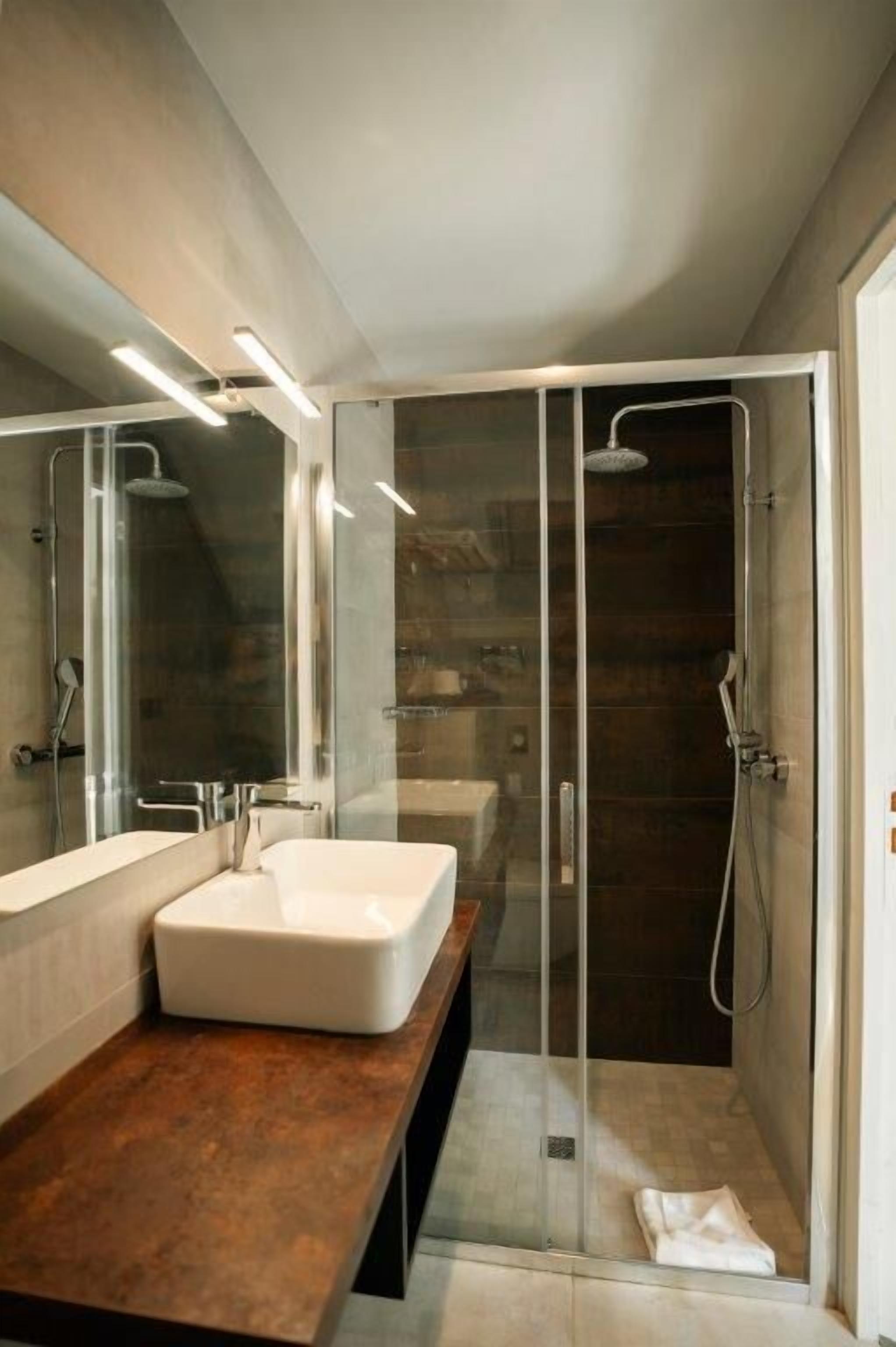 Un baño moderno con ducha de vidrio, un espejo grande y un tocador de madera.