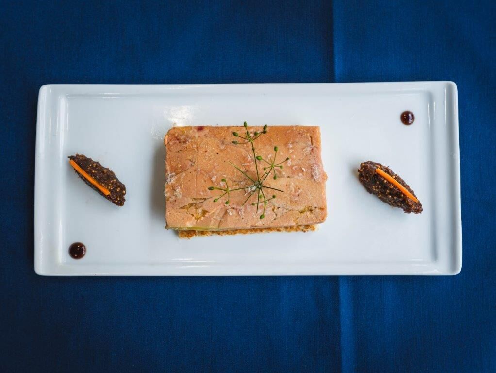 Un plato blanco rectangular con un alimento rectangular, adornado con una ramita de hierba y dos pequeños elementos decorativos a cada lado.