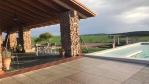 A covered outdoor area with stone pillars, a pool, and a view of a green field. - Yeguada farm El Corral Delconde (Fernán Caballero)