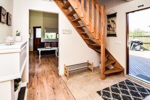 A staircase leading to a second floor, a white sofa, a small table, and a wooden bench in a room with wooden flooring and a tiled entrance. - House V10 (Bláskógabyggd)