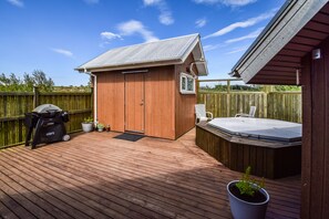 A wooden deck with a hot tub, a barbecue grill, and a small shed. - House V10 (Bláskógabyggd)
