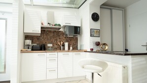 A modern kitchen with white cabinets, a microwave, a coffee maker, and a bar stool.