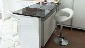 A modern kitchen with a central island, white bar stools, and a clock on the wall.