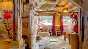 Ein rustikaler Innenraum mit freiliegenden Holzbalken, einem Kamin aus Stein und einem Fellteppich auf dem Boden.