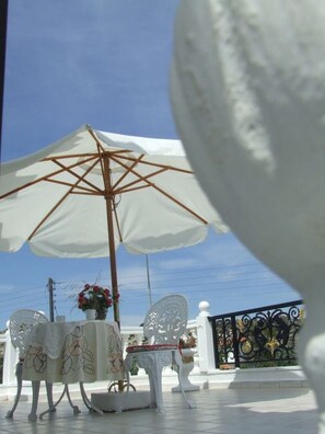 A terrace with a white umbrella, a table with chairs, and a decorative chair. - Castellino Studios - Twin Studio 8 (Faliraki)