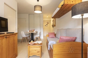 Une pièce chaleureuse avec un meuble TV en bois, une table à manger avec des chaises, un canapé avec des coussins et une lampe.
