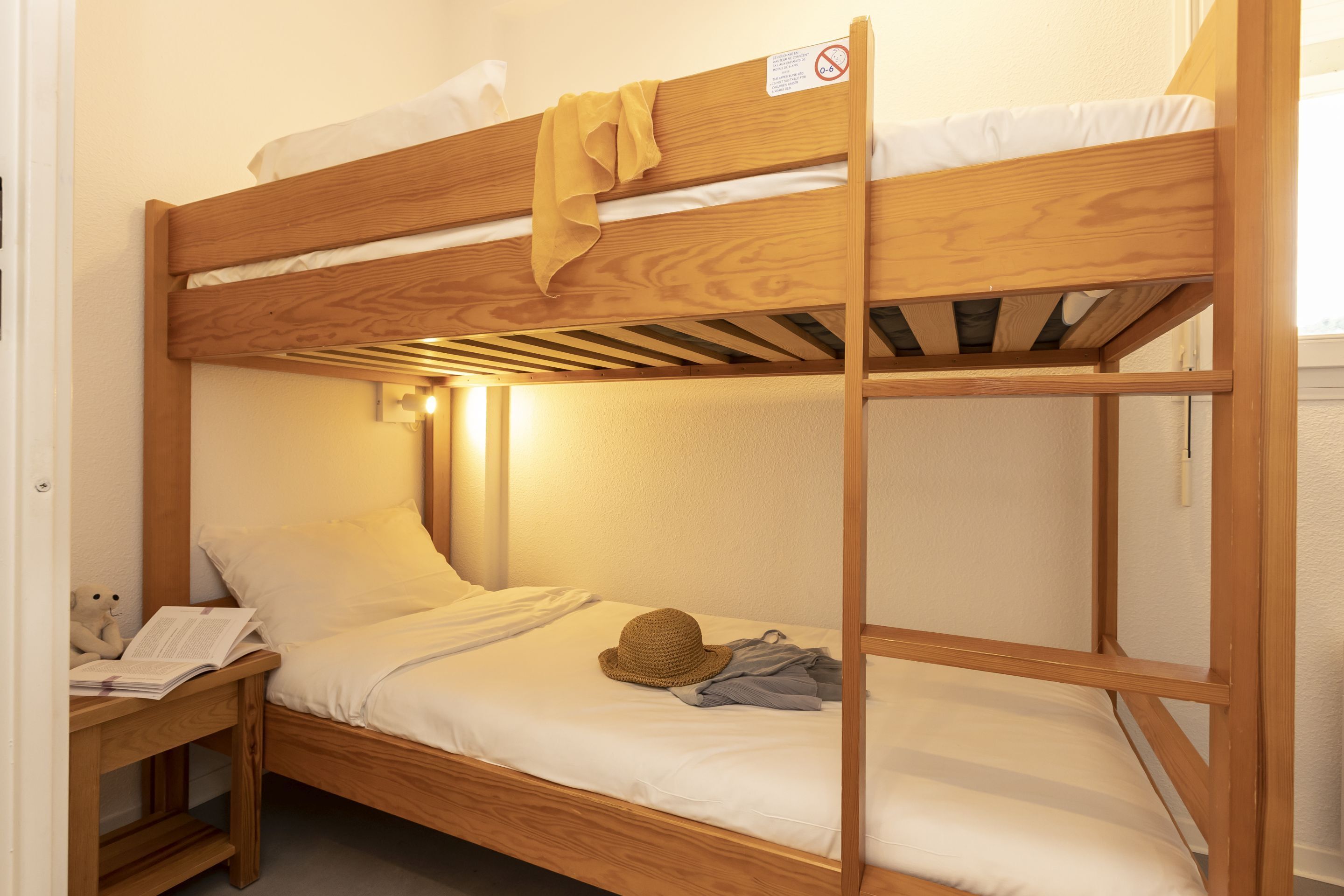 A bunk bed with a wooden frame, a pillow, a hat, and a book on the lower bunk.