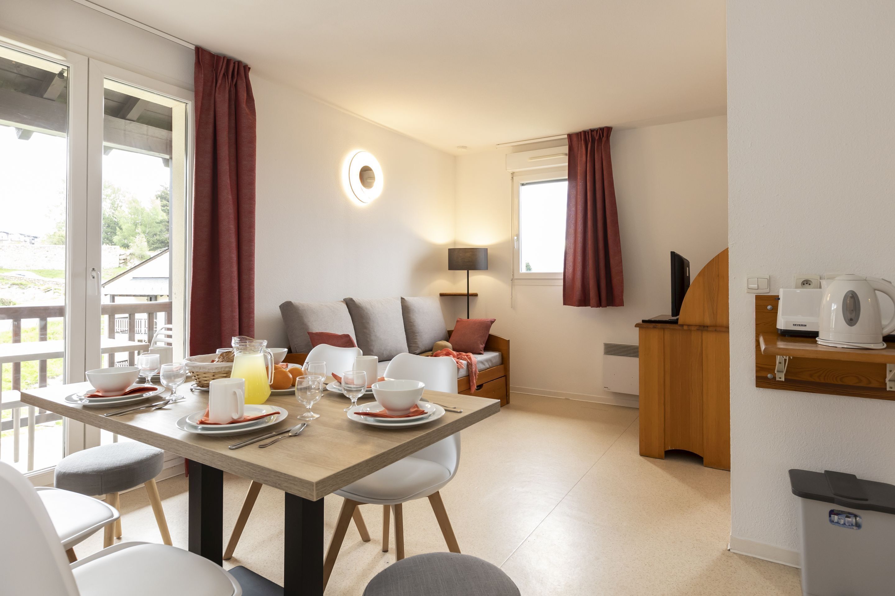 Une cuisine et un coin repas modernes, avec une table en bois dressée pour le petit-déjeuner, un canapé avec des coussins et une machine à café.