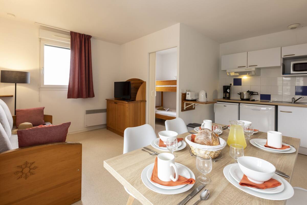 Une chambre d’hôtel moderne dotée d’un coin repas, d’une kitchenette et d’un espace salon confortable avec un téléviseur et des coussins.