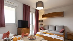 A hotel room with a bed, a TV, a dining table with breakfast items, and a window with curtains. - Résidence Odalys Mille Soleils (Font-Romeu-Odeillo-Via)