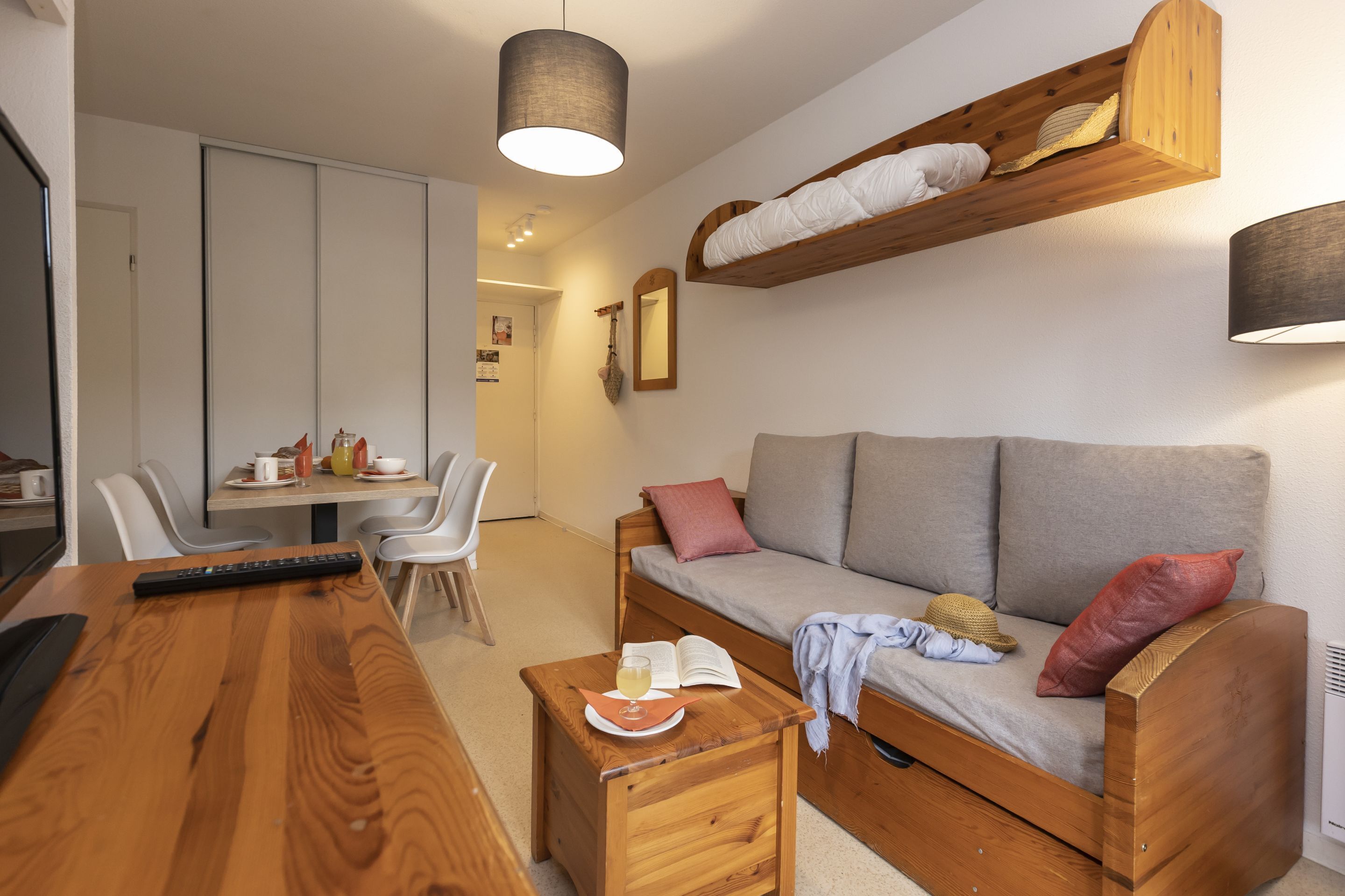 A cozy living area with a wooden sofa, a small wooden table with a book and a glass, and a dining table with chairs.