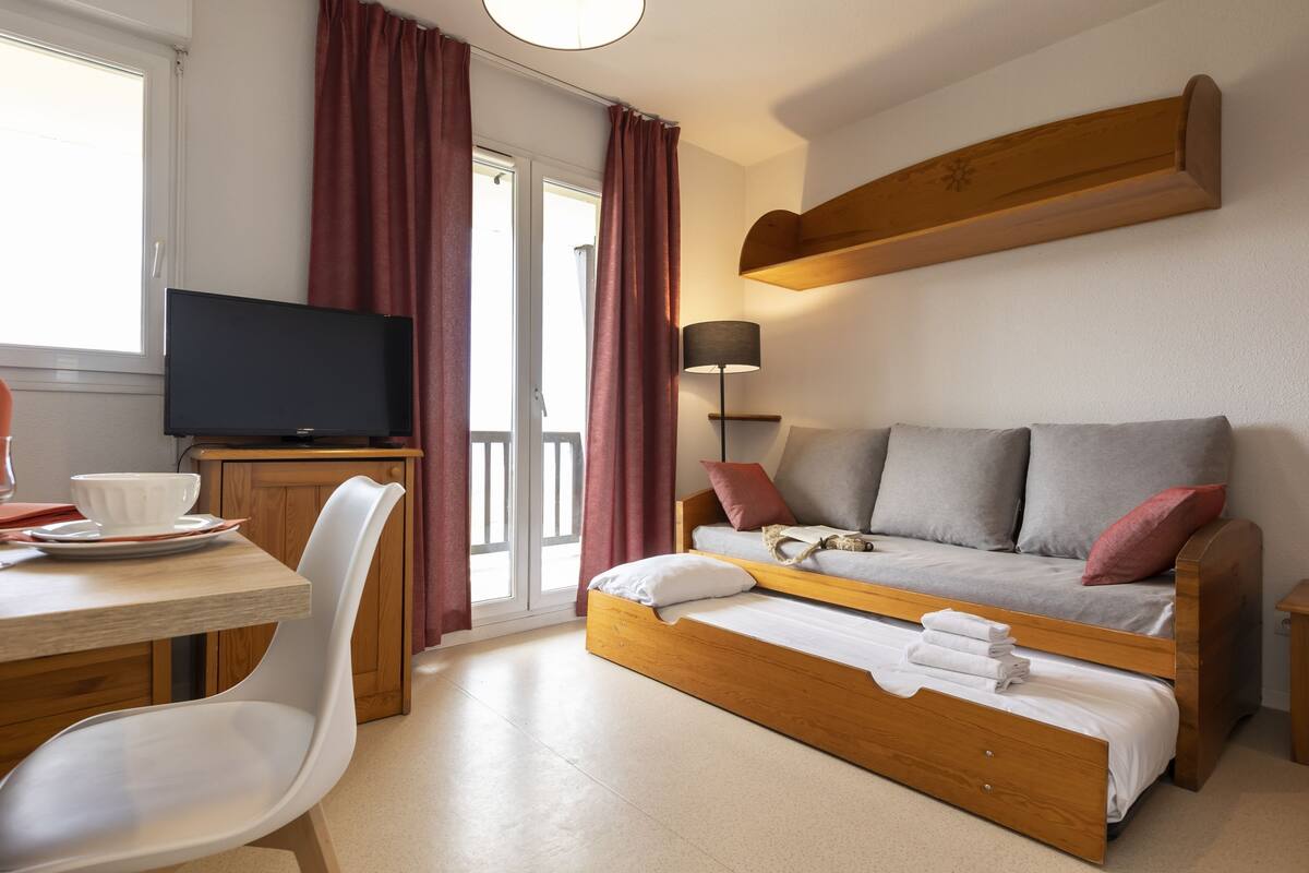 Une chambre avec un lit, une télévision, une table avec une chaise et une fenêtre avec des rideaux.