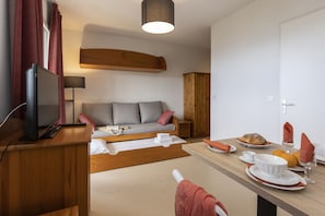 Une pièce moderne comprenant un canapé, un meuble en bois, une table à manger dressée avec des assiettes, des verres et un pain.