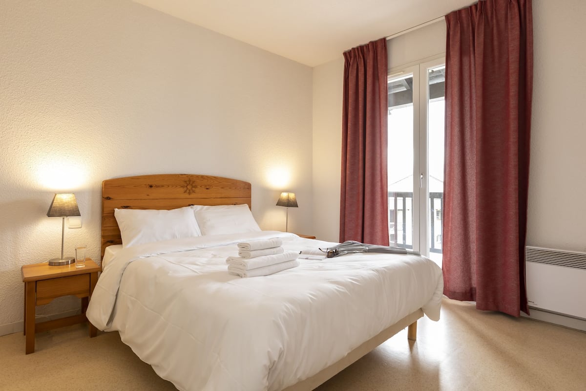 Un lit bien fait, avec du linge de lit blanc, une tête de lit en bois et deux lampes de chevet.