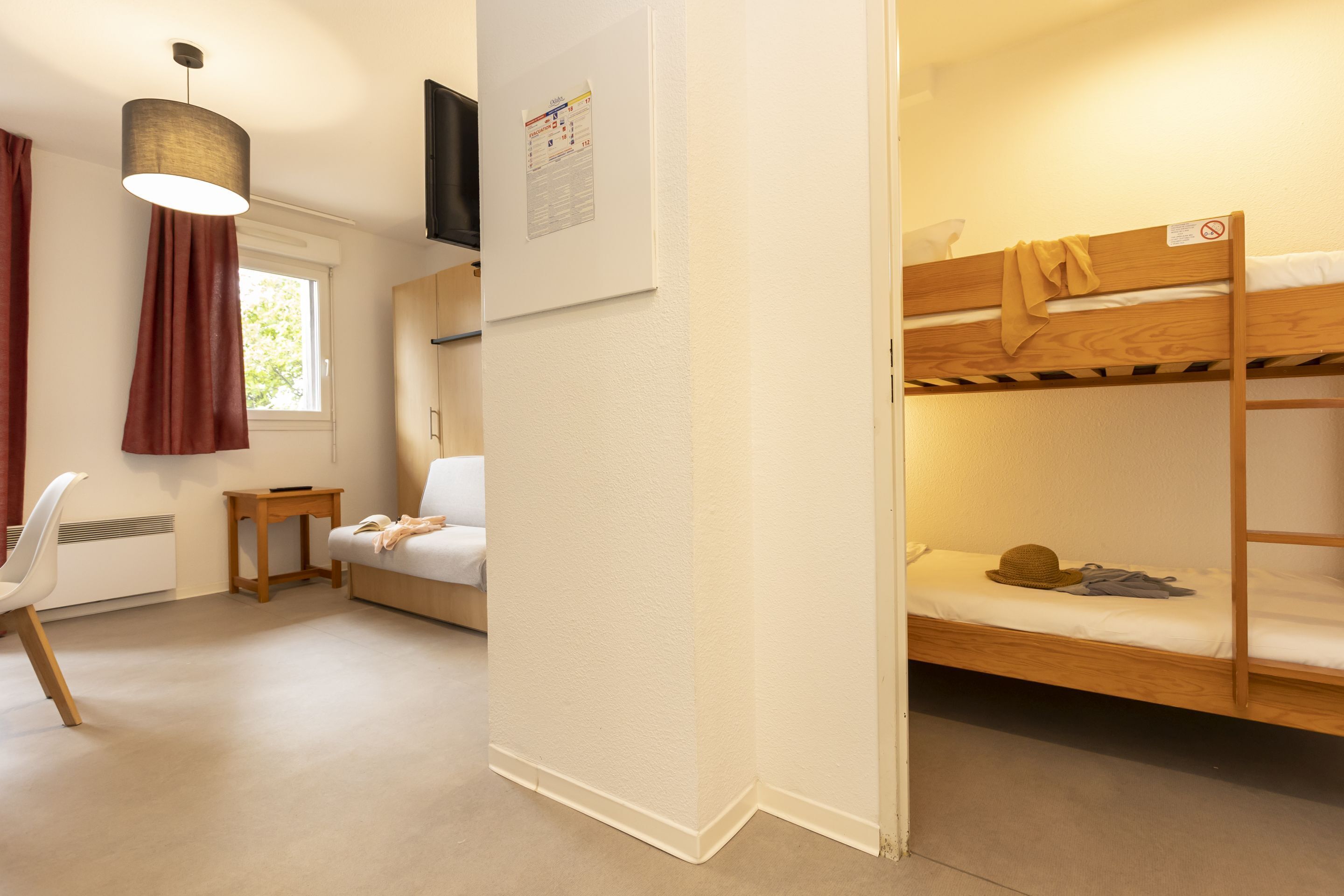 A dormitory room with bunk beds, a white sofa, a small table, and a hanging light fixture.
