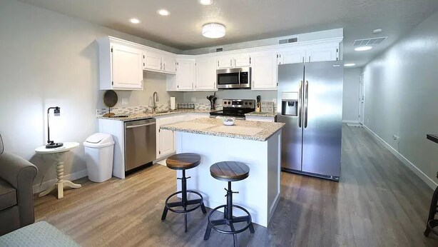 A modern kitchen with white cabinets, stainless steel appliances, a granite countertop, and two bar stools. - Beautifully Remodeled Condo - Fountain Views (St. George)