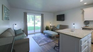 A modern living room with a sofa, a small table, and a kitchen area with a countertop and cabinets. - Beautifully Remodeled Condo - Fountain Views (St. George)