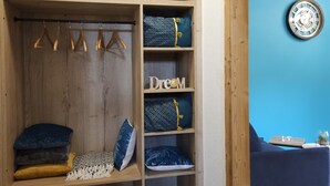 A wooden wardrobe with multiple shelves, a hanging rod, and a blue accent wall with a clock. - Gite "Bleuet", the little LOFT, 2 to 6 persons with SPA in the Residence  (Ventron)