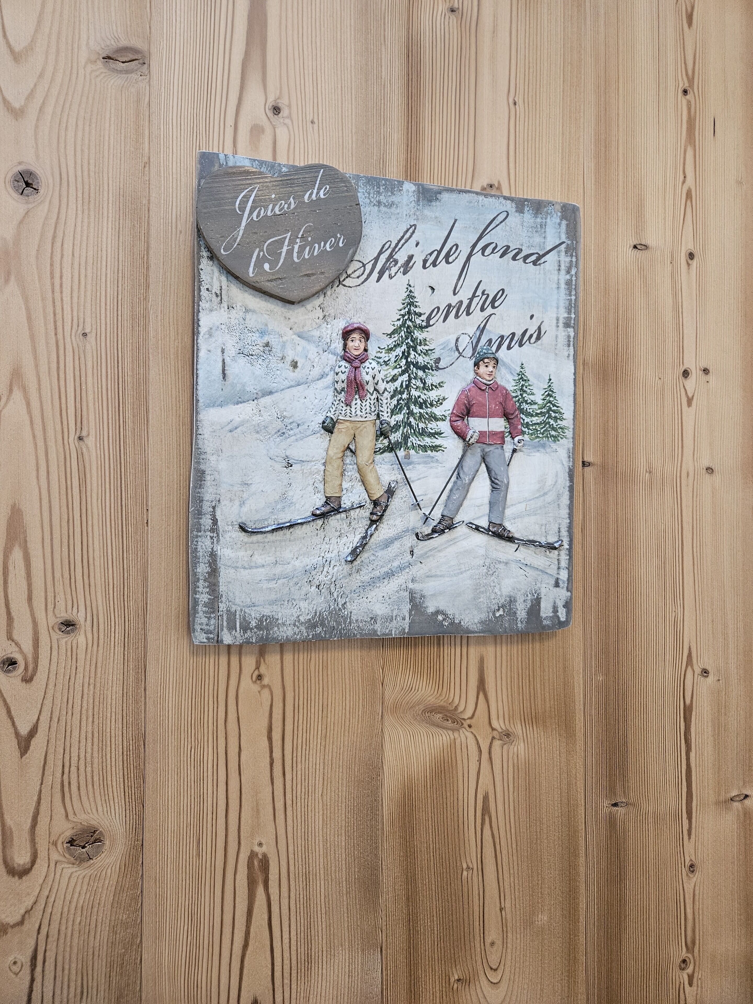 A wooden wall with a decorative plaque featuring a winter scene with two skiers and a snow-covered mountain.