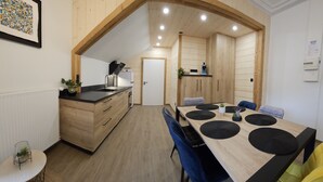A modern kitchen with wooden cabinets, a black countertop, and a sink. There is a dining area with a wooden table and blue chairs. - Gite "Bleuet", the little LOFT, 2 to 6 persons with SPA in the Residence  (Ventron)