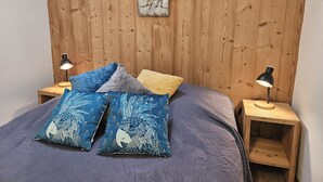 A bedroom with a wooden headboard, a bed with blue and gray bedding, and two bedside tables with lamps. - Gite "Bleuet", the little LOFT, 2 to 6 persons with SPA in the Residence  (Ventron)