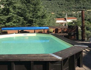A swimming pool with a wooden deck and a blue tarp.