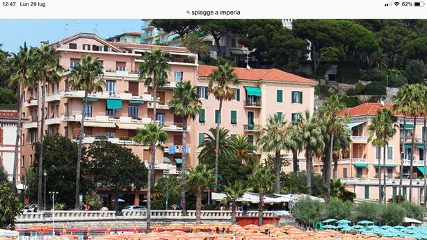 Una playa con filas de tumbonas y sombrillas, un edificio con balcones y palmeras.