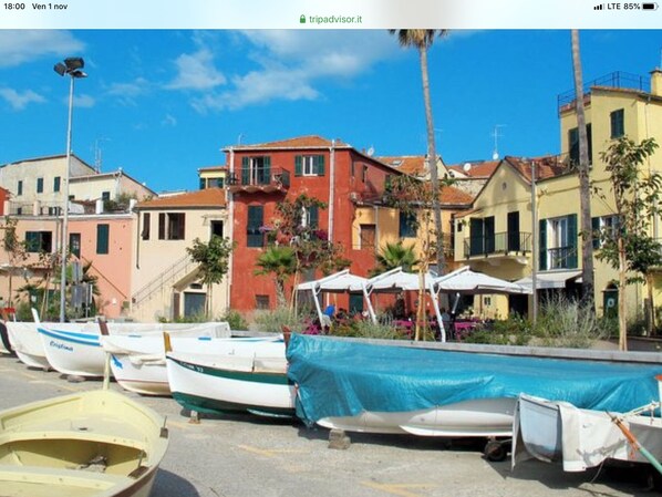 Une rangée de bateaux est amarrée le long d’une promenade, avec des bâtiments aux couleurs vives en arrière-plan.