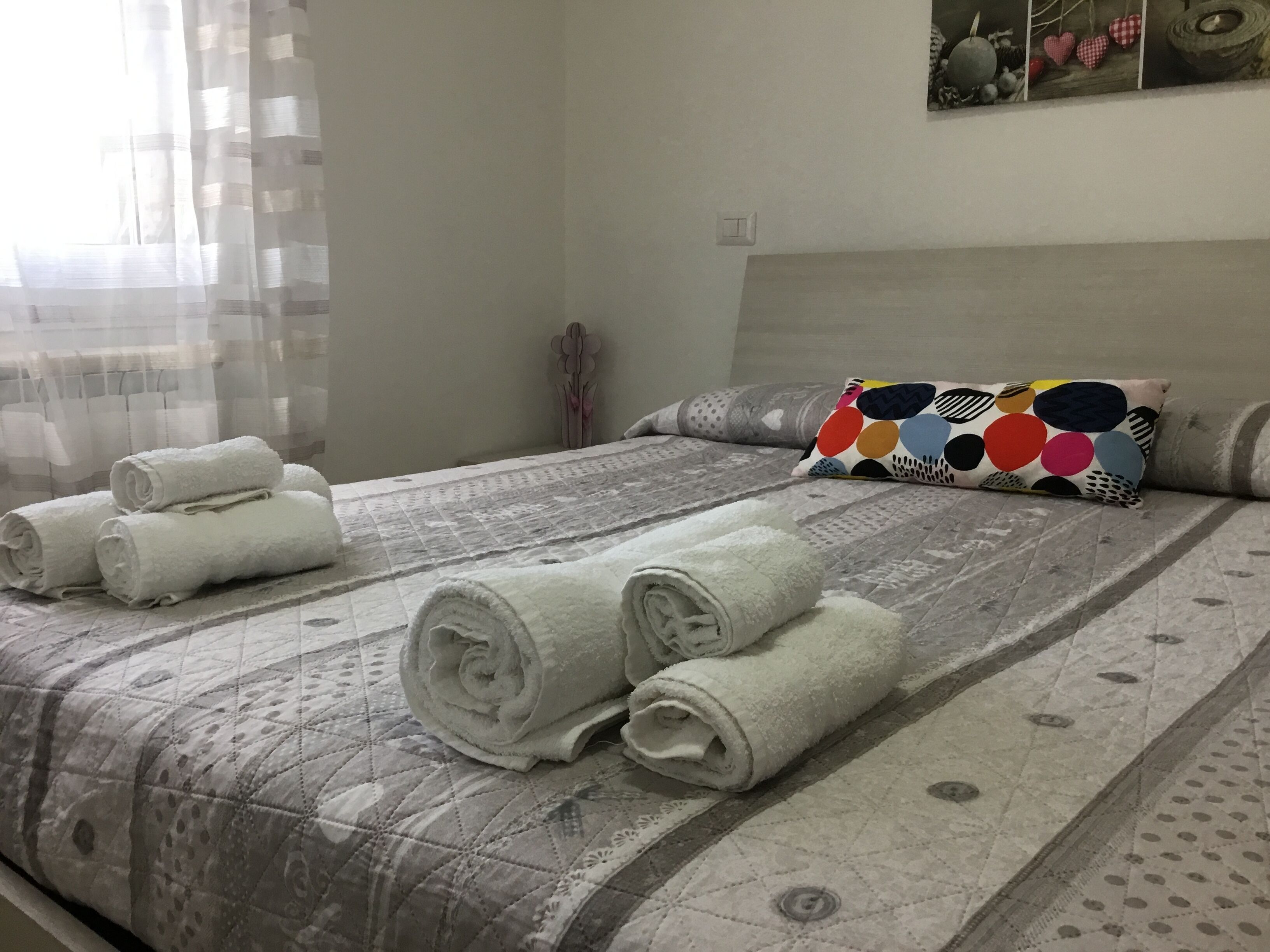A neatly made bed with rolled white towels, a patterned quilt, and a colorful pillow.